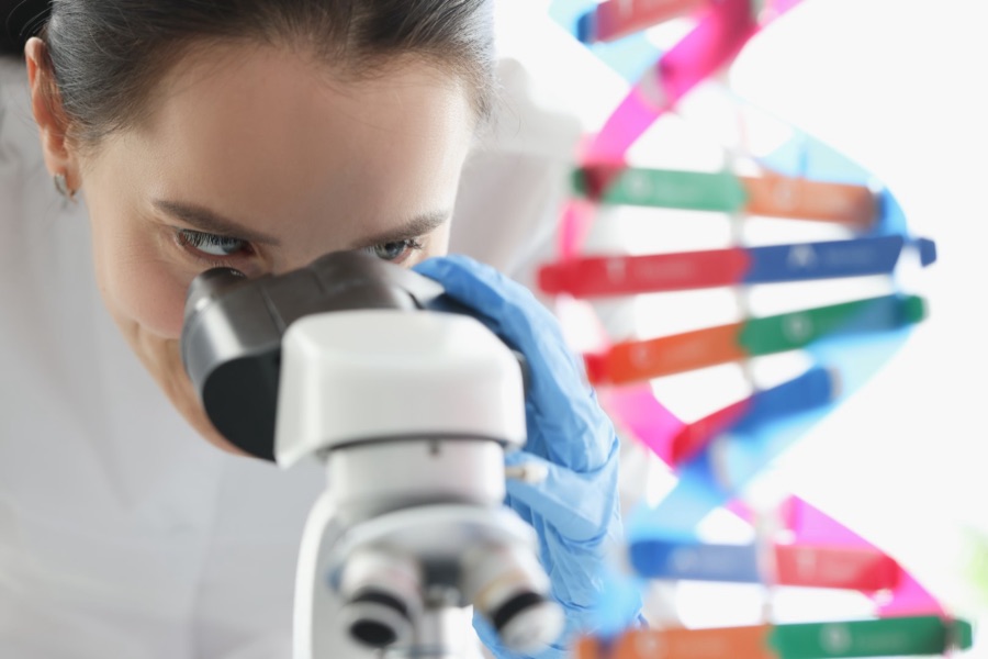 Científica al microscopio junto a un modelo de ADN