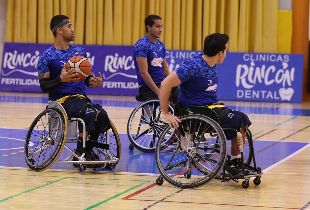 Tres jugadores de baloncesto en silla de ruedas disputan el balón ante la publicidad de Clínicas Rincón