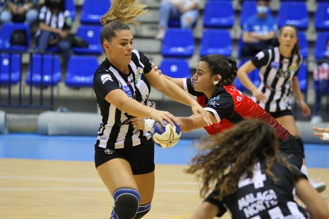 Lance de un partido de balonmano femenino: una jugadora protege el balón ante dos rivales