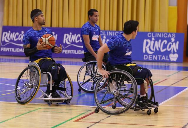 Tres jugadores de baloncesto en silla de ruedas disputan el balón ante la publicidad de Clínicas Rincón