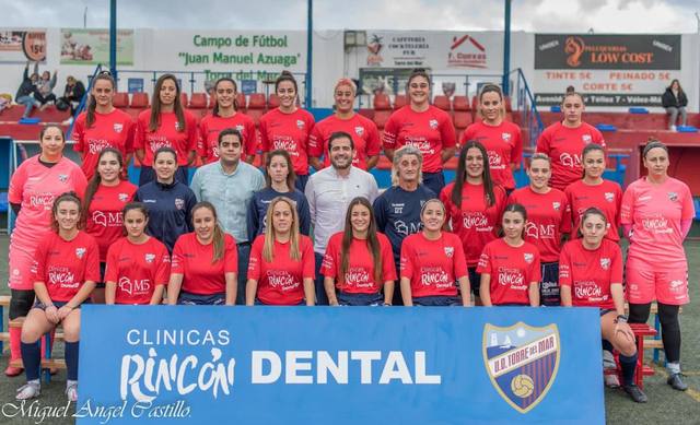 Plantilla del equipo femenino de la U.D. Torre del Mar en el campo Juan Manuel Azuaga, con la valla de Clínicas Rincón Dental