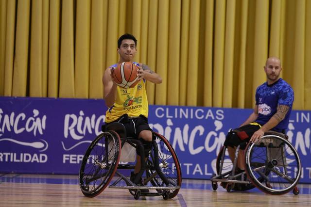Dos jugadores de baloncesto en silla de ruedas ante las vallas de Clínicas Rincón Dental y Rincón Fertilidad
