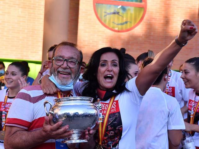 Celebración con el trofeo en el pabellón, rodeados por las jugadoras del equipo