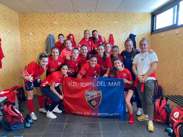 Plantilla femenina de la U.D. Torre del Mar posa en el vestuario con la bandera del club