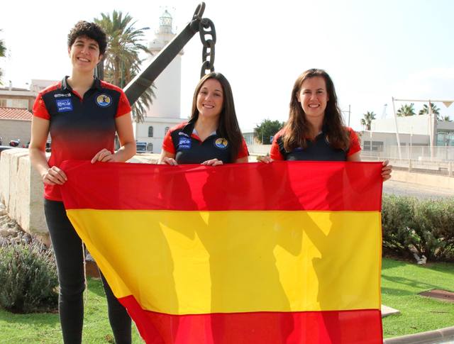 Tres jugadoras sostienen una bandera de España junto al faro