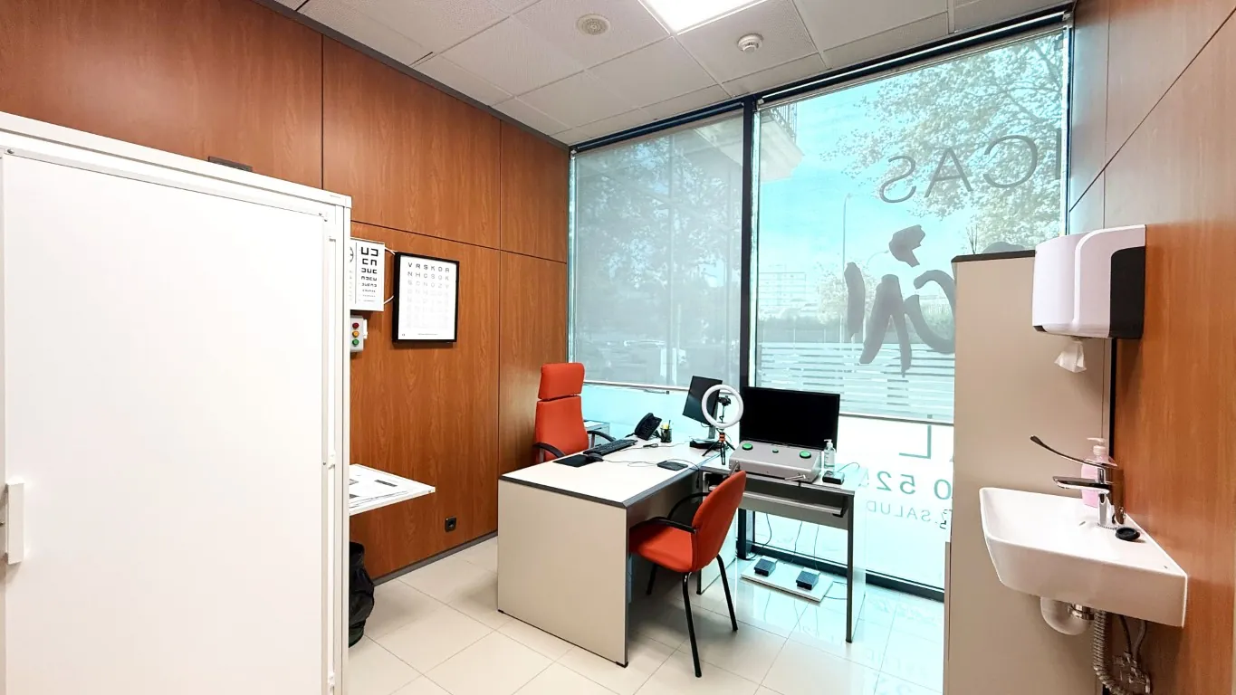 Consulta médica con mesa de trabajo, ordenador y lavabo