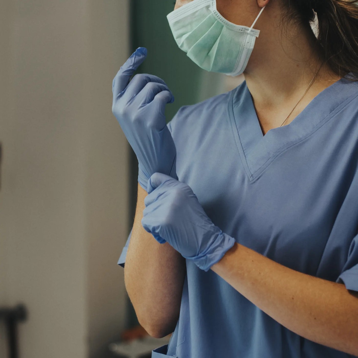 Profesional de enfermería con pijama sanitario azul y mascarilla poniéndose unos guantes